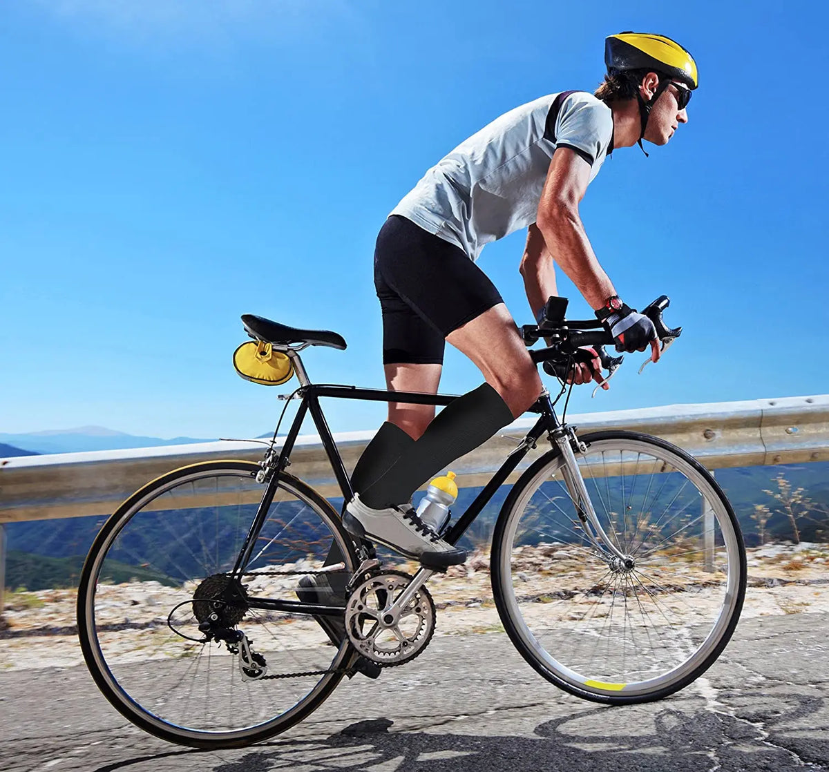 A man riding a bicycle outdoors wearing compression socks and a yellow helmet.
