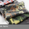 A stack of iced silk fabric in various camouflage patterns, including orange and black, olive green, and gray.