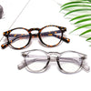 A pair of orange and black patterned square frame glasses resting on a white surface with green leaves.