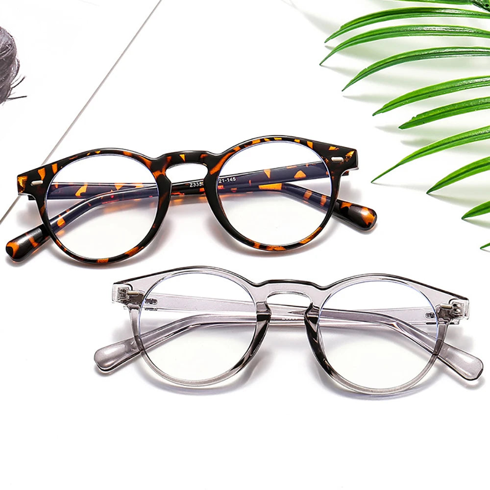 A pair of orange and black patterned square frame glasses resting on a white surface with green leaves.