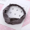 Un bandeau élastique gris torsadé et noué, présenté sur fond blanc avec le mot LOVE en motif de grille.