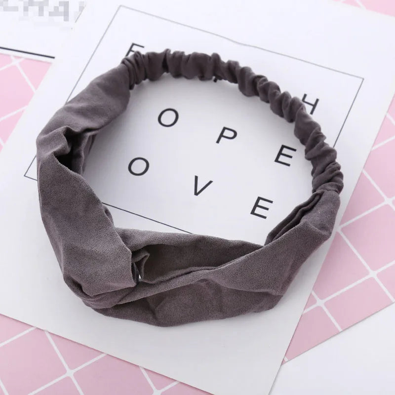 Un bandeau élastique gris torsadé et noué, présenté sur fond blanc avec le mot LOVE en motif de grille.
