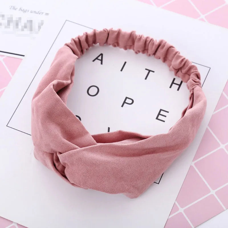 Un bandeau élastique torsadé rose poudré pour bébé fille, sur fond blanc.