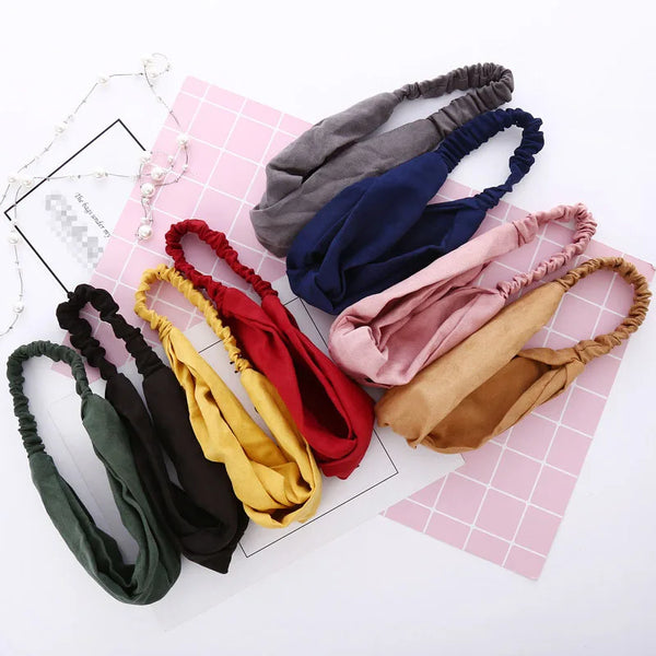 A collection of twisted knotted elastic headbands in various shades of gray, blue, pink, red, and olive green laid on pink pa