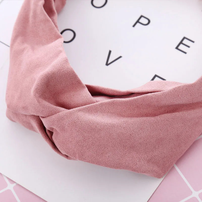 Un bandeau élastique torsadé rose poudré, drapé sur une surface blanche.