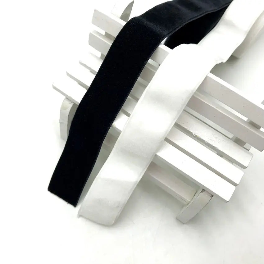 Black and white stretch velvet elastic headbands displayed on a white wooden or plastic rack.
