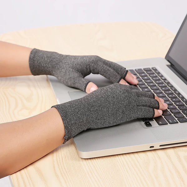 A hand wearing a gray compression glove is typing on a silver laptop keyboard.