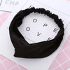 Un bandeau élastique noir torsadé et noué, présenté sur une surface blanche avec des accents roses.
