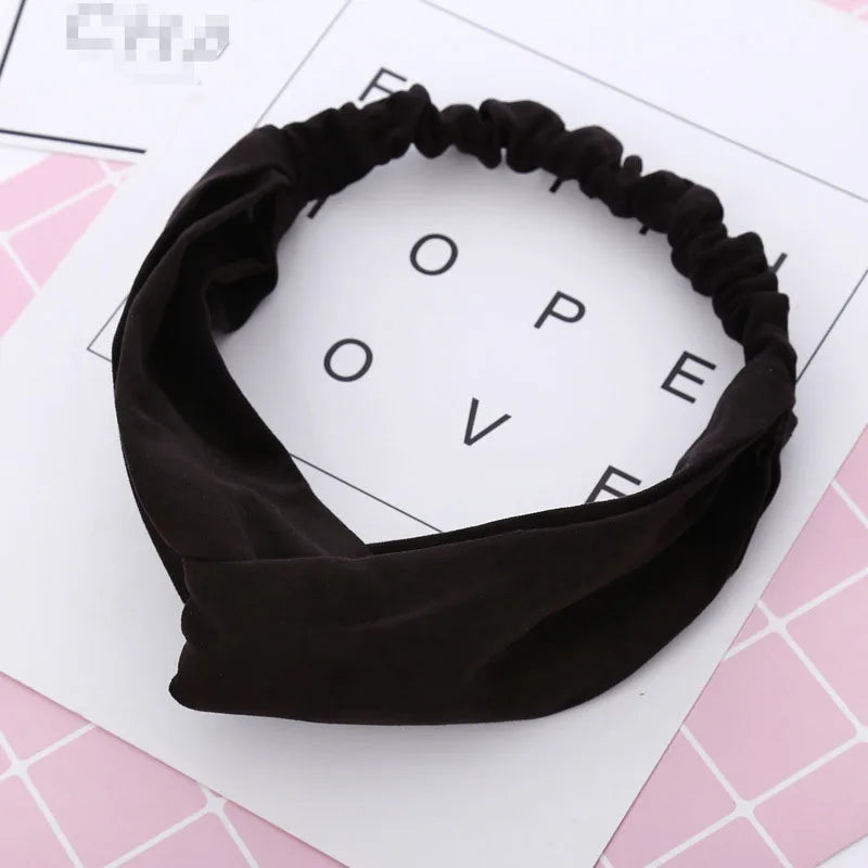 Un bandeau élastique noir torsadé et noué, présenté sur une surface blanche avec des accents roses.