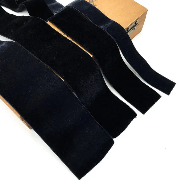 A set of black stretch velvet elastic headbands resting on a brown cardboard box.