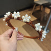 A close-up of a brown, ornate headband decorated with white pearls and rhinestones being held by a hand.