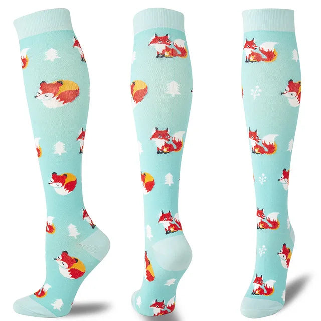 A set of multi-color compression socks featuring a pattern of red and orange cats and white Christmas trees on a light blue b