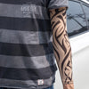 A person wearing a gray striped shirt and black tattoo arm sleeves.