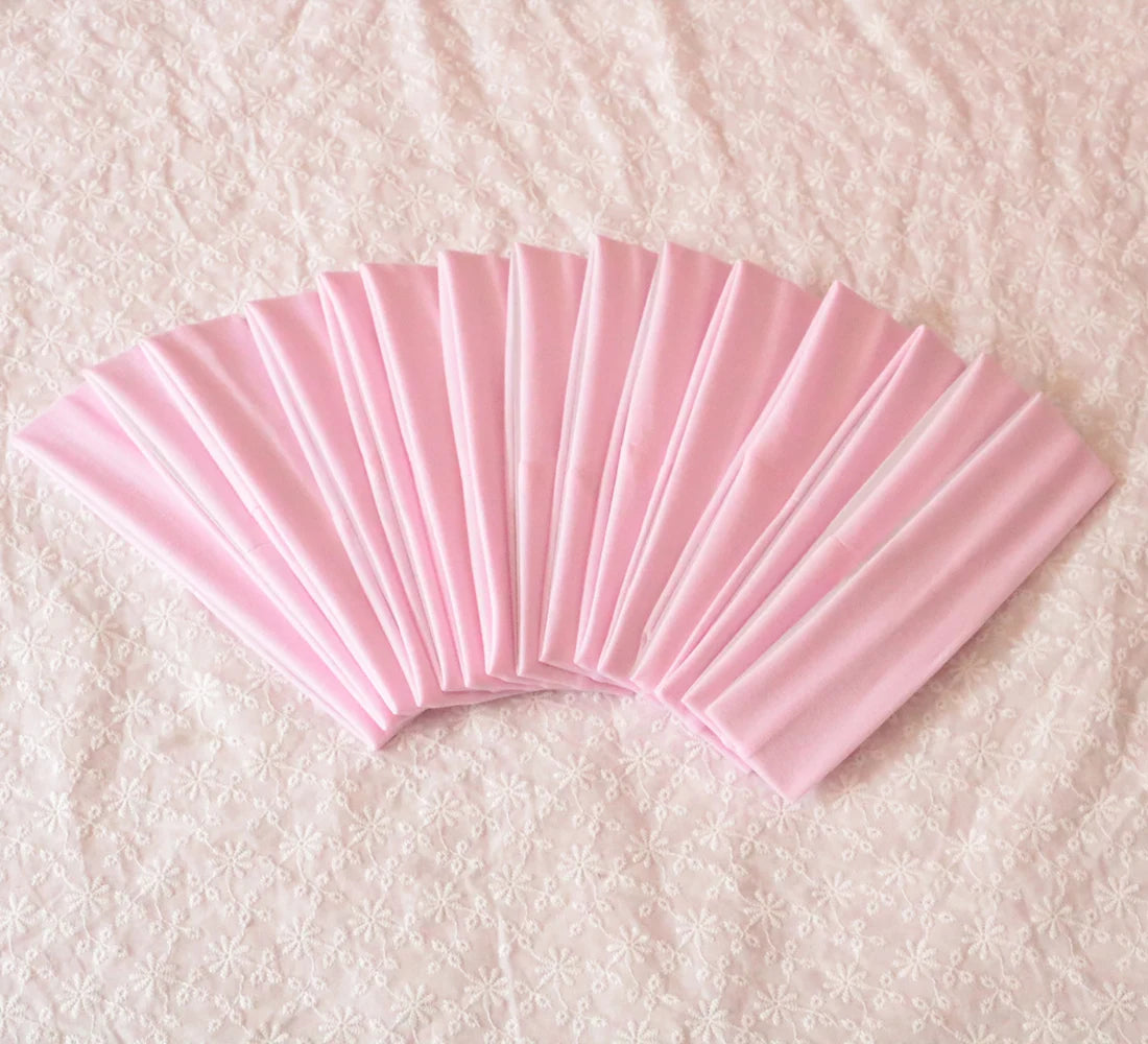 A fan of pink elastic headbands for sports and hair, shown fanned out on a light pink surface.