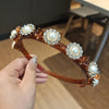 A hand holds an ornate, gold-toned headband decorated with pearl and rhinestone clusters.