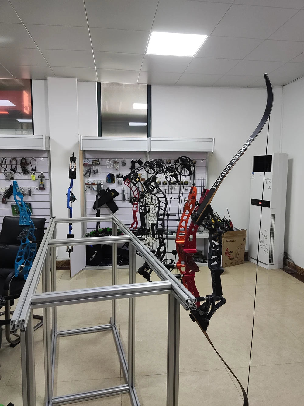 A set of lighted arrow nocks and an archery bow are displayed on a metal rack in a brightly lit room.