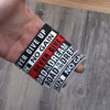 A hand holds several motivational silicone elastic bracelets with text like Ever Give Up and No Gain.