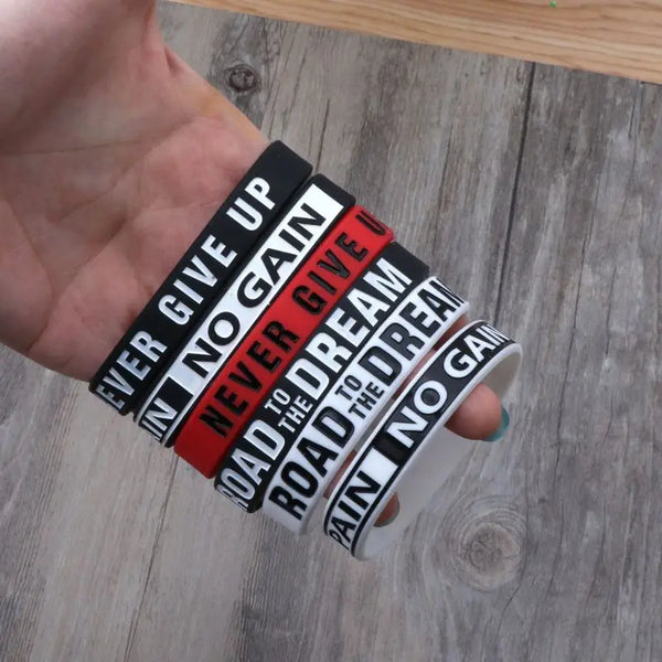 A hand holds several motivational silicone elastic bracelets with text like Ever Give Up and No Gain.