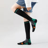 Calcetines de compresión médicos negros con dedos estampados en verde y naranja, puestos en la pierna de una persona.
