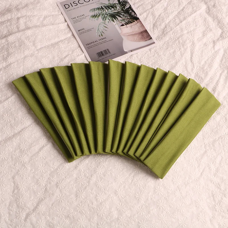 A fan of olive green elastic headbands is displayed next to a product packaging featuring tropical fern illustrations.