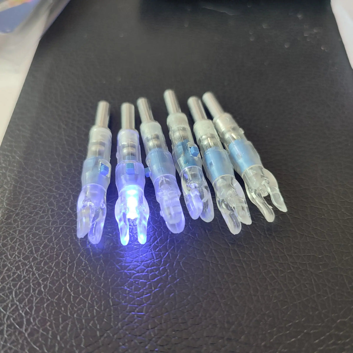 A row of lighted arrow nocks for archery, glowing blue in a dark setting.