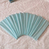 A fan of light blue satin elastic headbands arranged in a pleated fan shape on a pink textured surface.