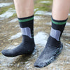 A pair of black waterproof breathable hiking socks with neon green trim standing in flowing water.