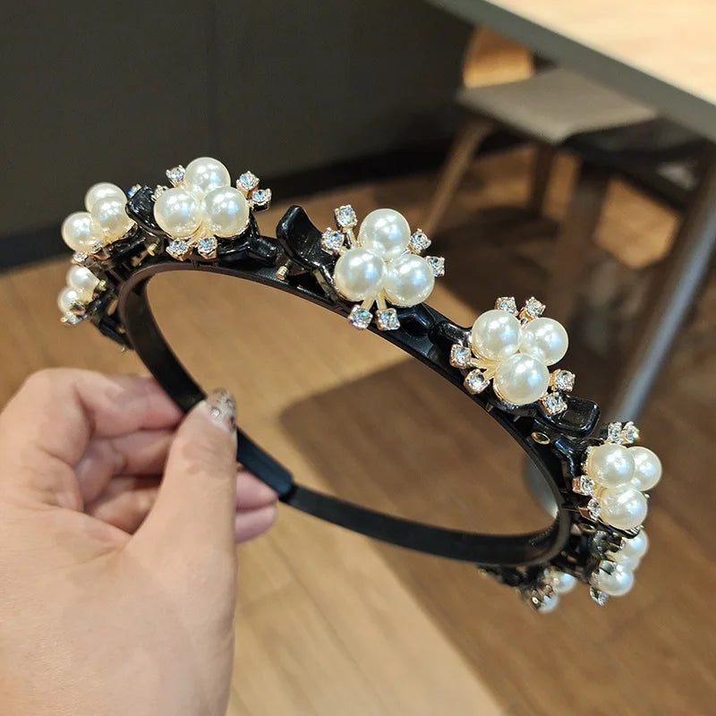 A black headband decorated with white pearls and clear rhinestones being held by a hand.