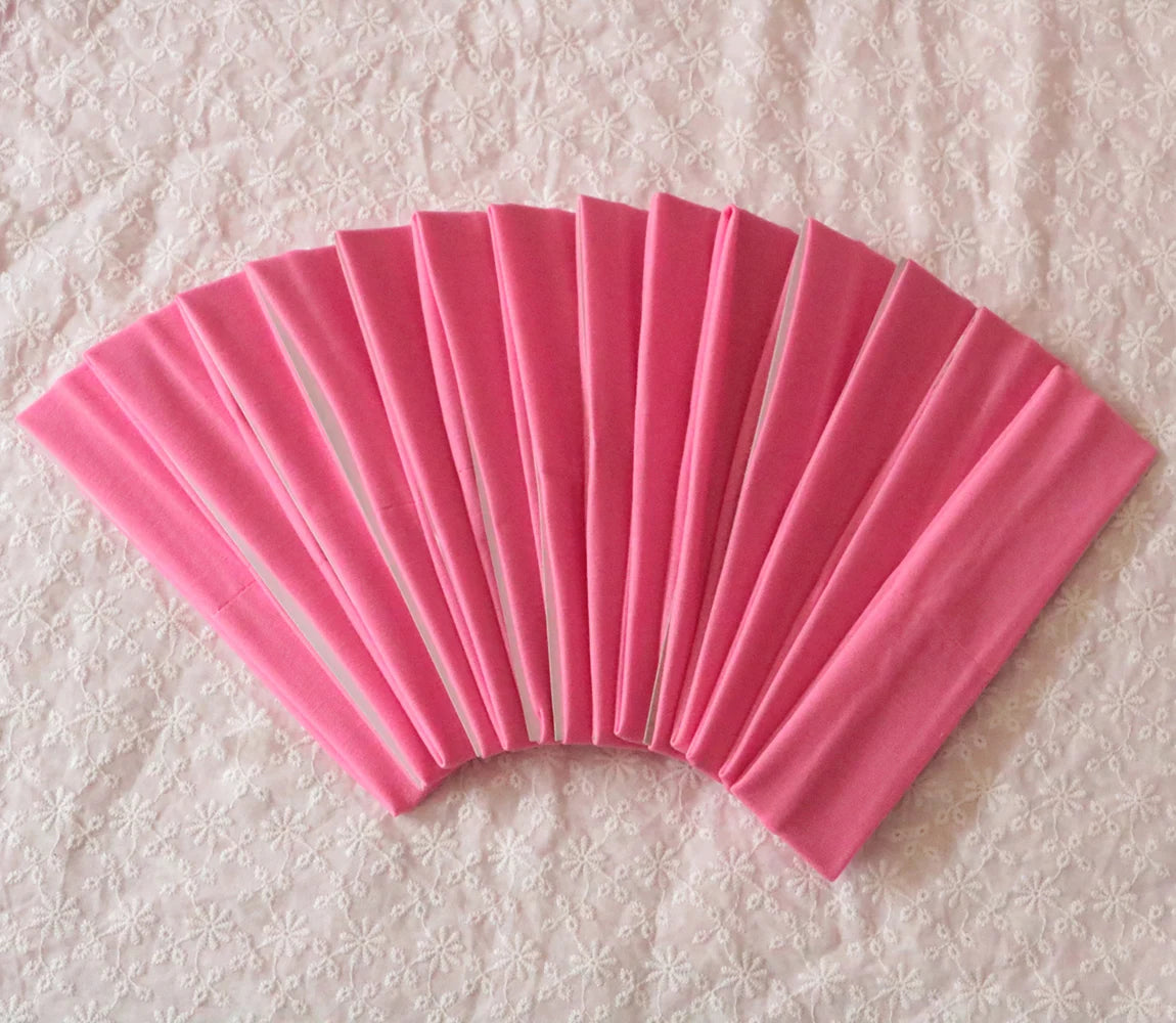 A fan of pink elastic headbands arranged in a semi-circle on a white textured surface.