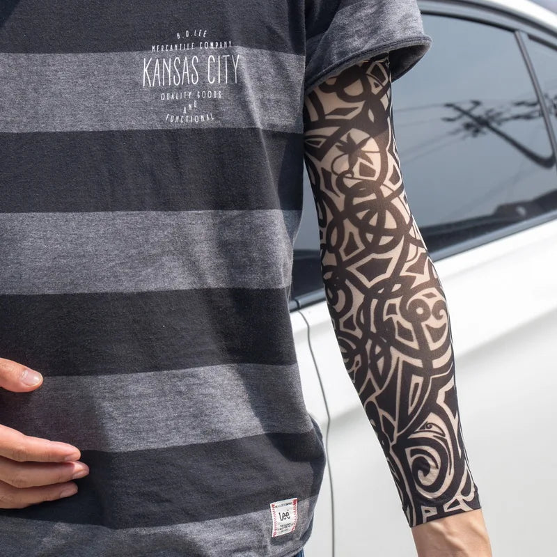 A person wearing a gray t-shirt with text and black geometric tattoo sleeves on their arm.