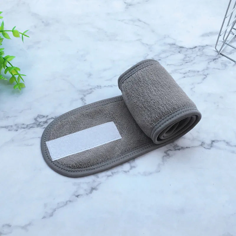A gray adjustable wide headband for hair, makeup, or spa use is shown on a white marble surface.