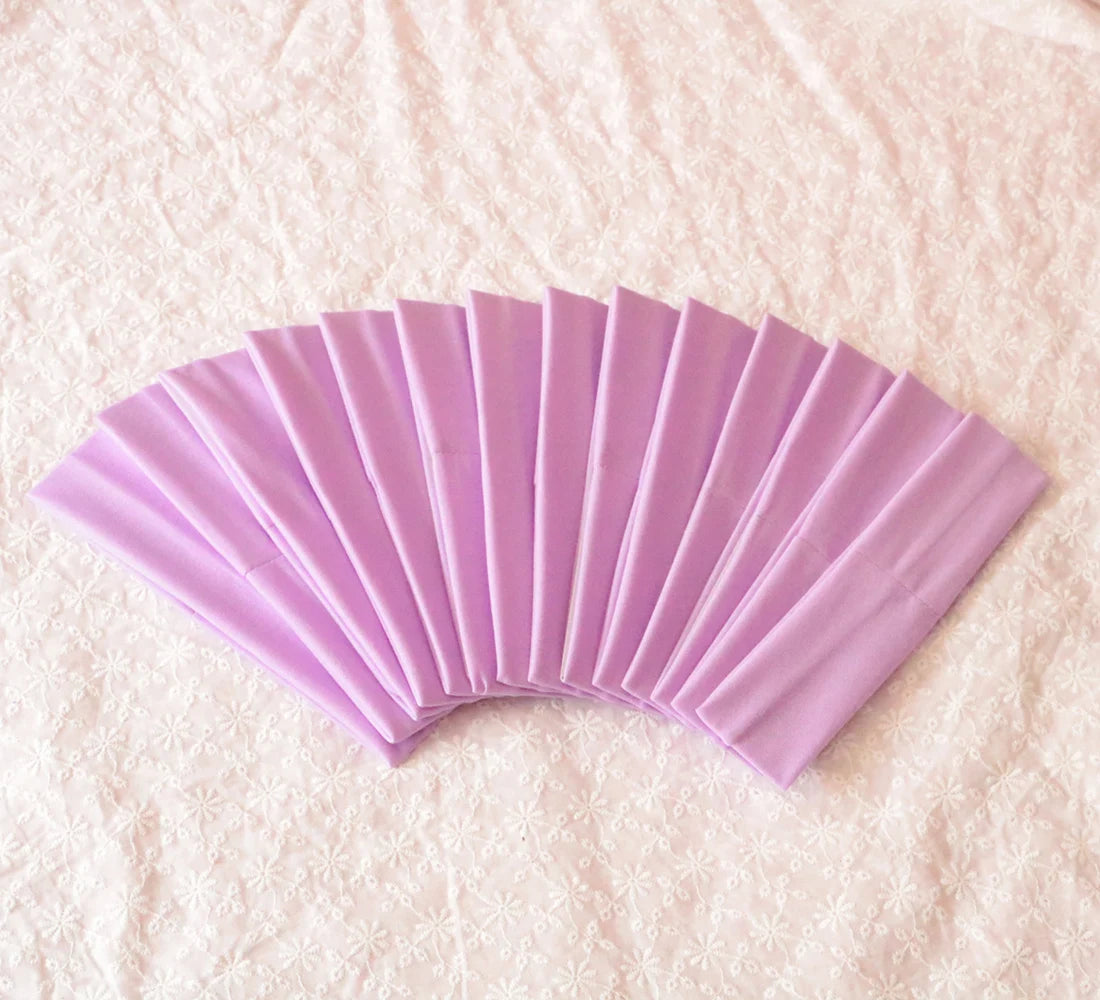 A fan of light purple elastic headbands arranged in a semi-circle on a white textured fabric.