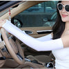 A woman wearing white fingerless arm sleeves is driving a car, holding the steering wheel.
