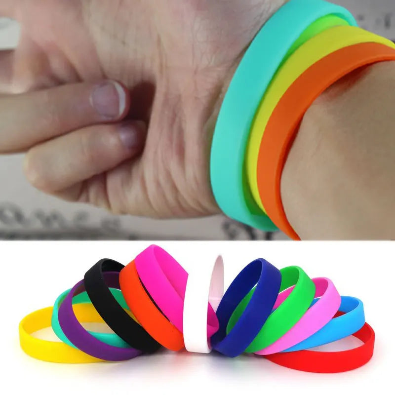 A hand is wearing a stack of multi-color silicone elastic wristbands in shades of green, orange, yellow, and pink.