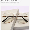 Un par de gafas con montura de metal dorado y lentes transparentes sobre una superficie blanca.