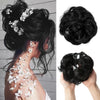 A woman's dark hair styled in a messy curly bun with white floral extensions.