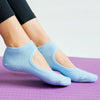 Light blue breathable women's pilates and yoga socks worn on feet against a purple surface.