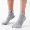 A pair of grey ankle socks featuring the Champion logo and blue text on the heel.