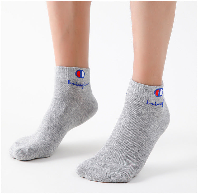 A pair of grey ankle socks featuring the Champion logo and blue text on the heel.