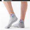 A pair of grey ankle socks with blue and red embroidered logos are shown on a person's lower leg.