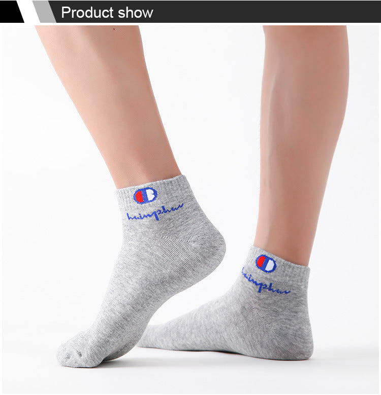 A pair of grey ankle socks with blue and red embroidered logos are shown on a person's lower leg.