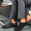 A close-up of a person wearing black dress shoes and black no-show socks while sitting down.