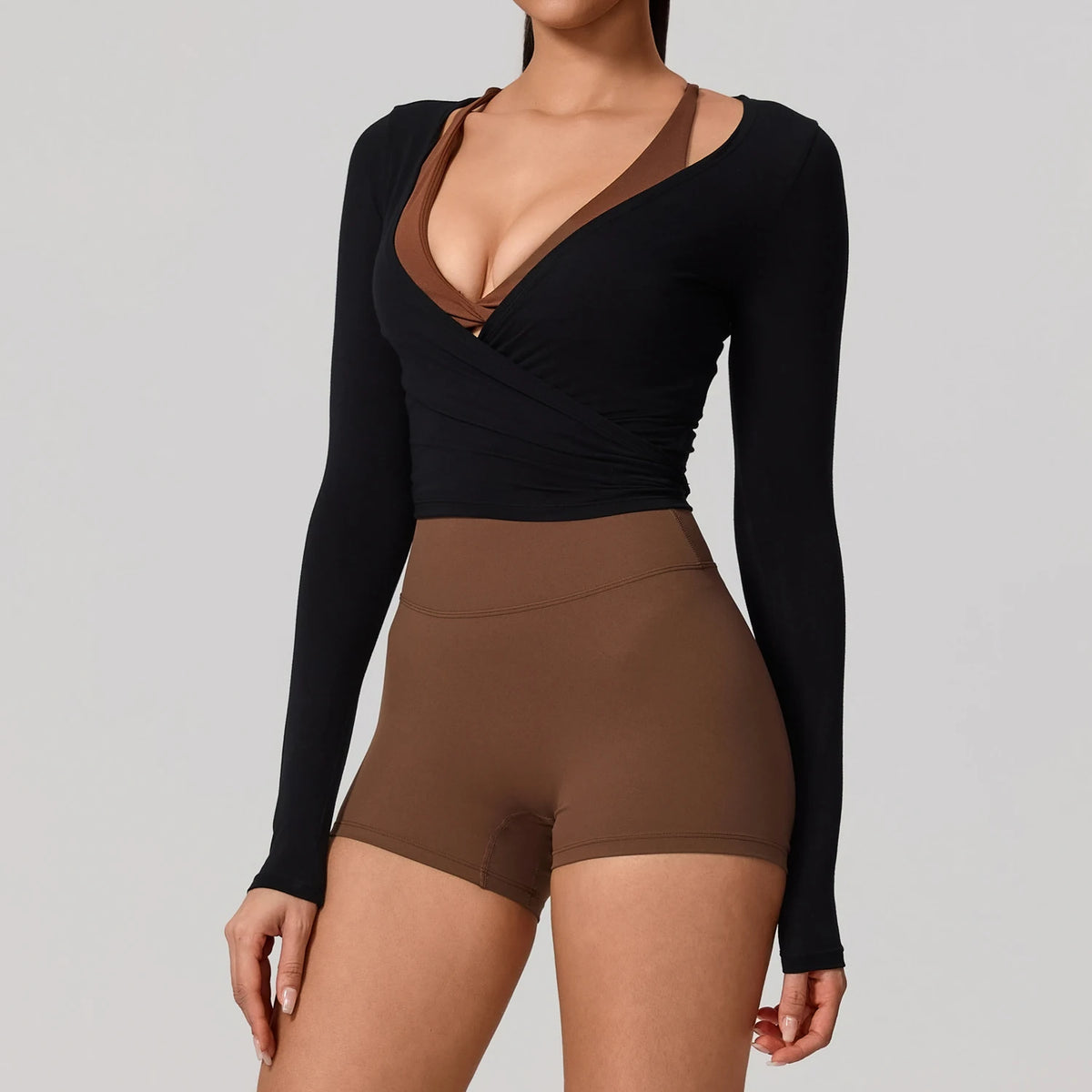 A woman wearing a black long sleeve top with a brown V-neck and matching high-waisted bottoms.