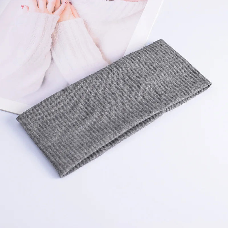 A gray knitted headband is shown next to pink knitted fabric and fingers on a white background.