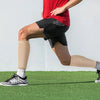 A person wearing red a shirt and black shorts is exercising while wearing tan calf compression sleeves.