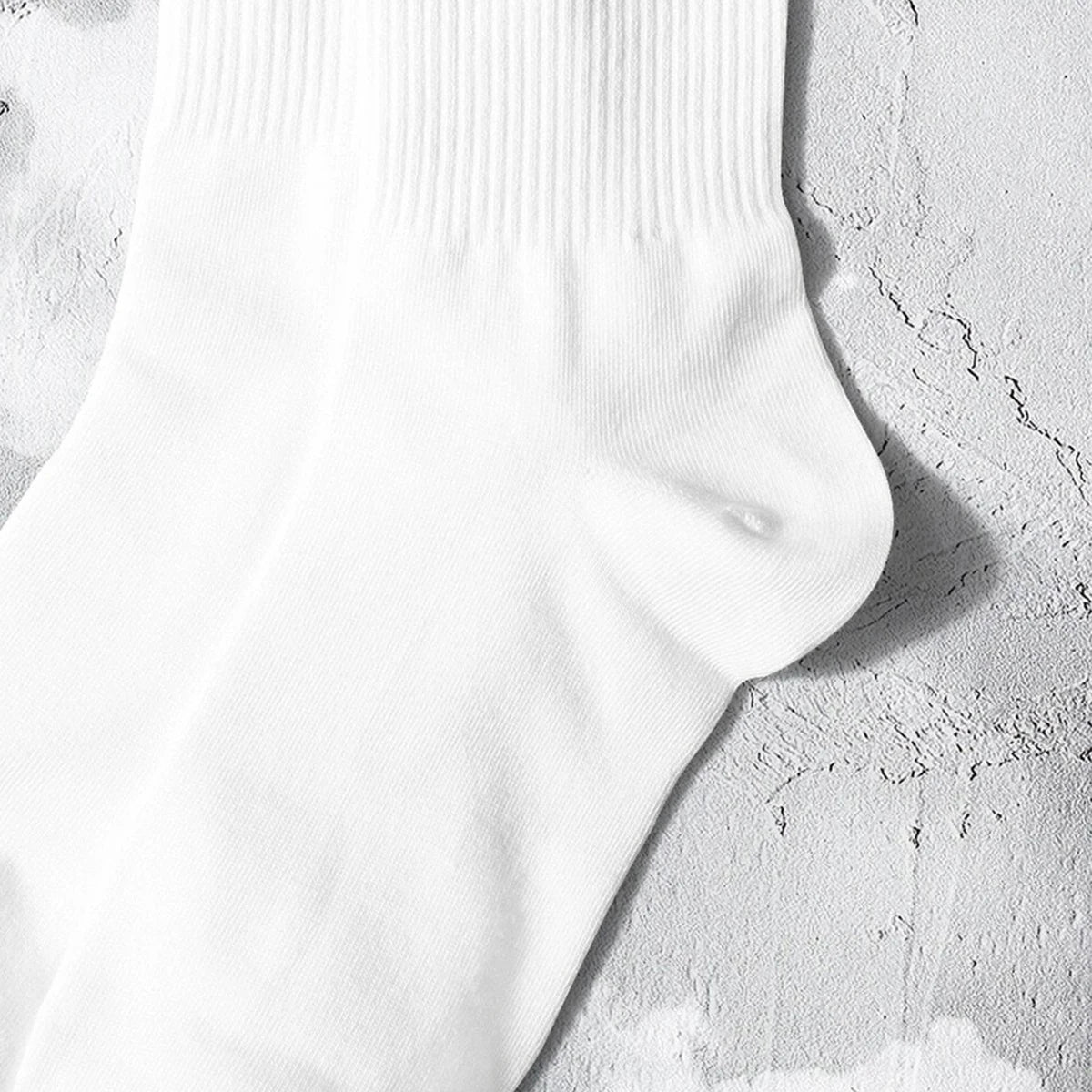 A close-up of a white crew sock with subtle vertical ribbing and a small mark on the ankle area.