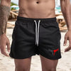 A muscular man wearing black quick-drying swim shorts on a beach.