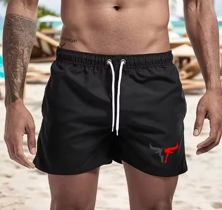 A muscular man wearing black quick-drying swim shorts on a beach.