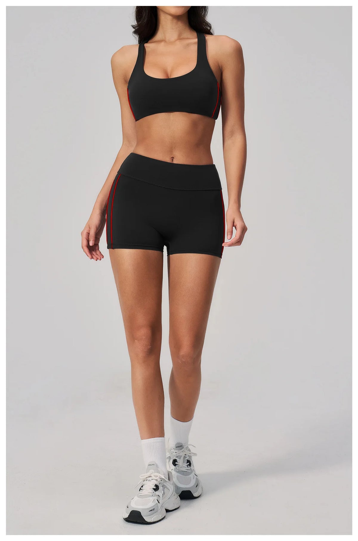 A woman models a black two-piece yoga and sports tracksuit set with red trim.