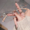 A hand holds a pair of thin, rose gold anti-blue light reading glasses with light wood accents against a blurred background.